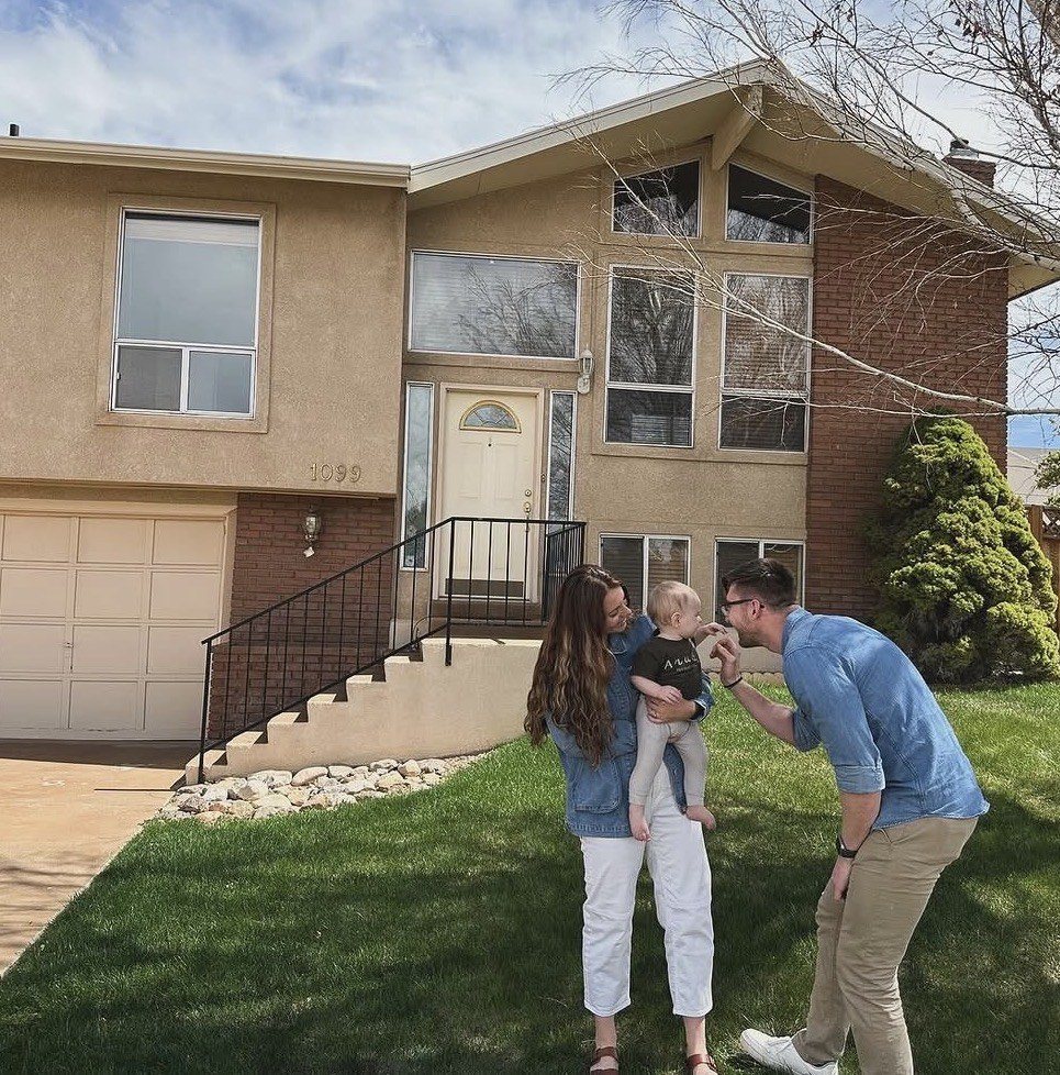 Brian and his wife holding their child in front of their first home